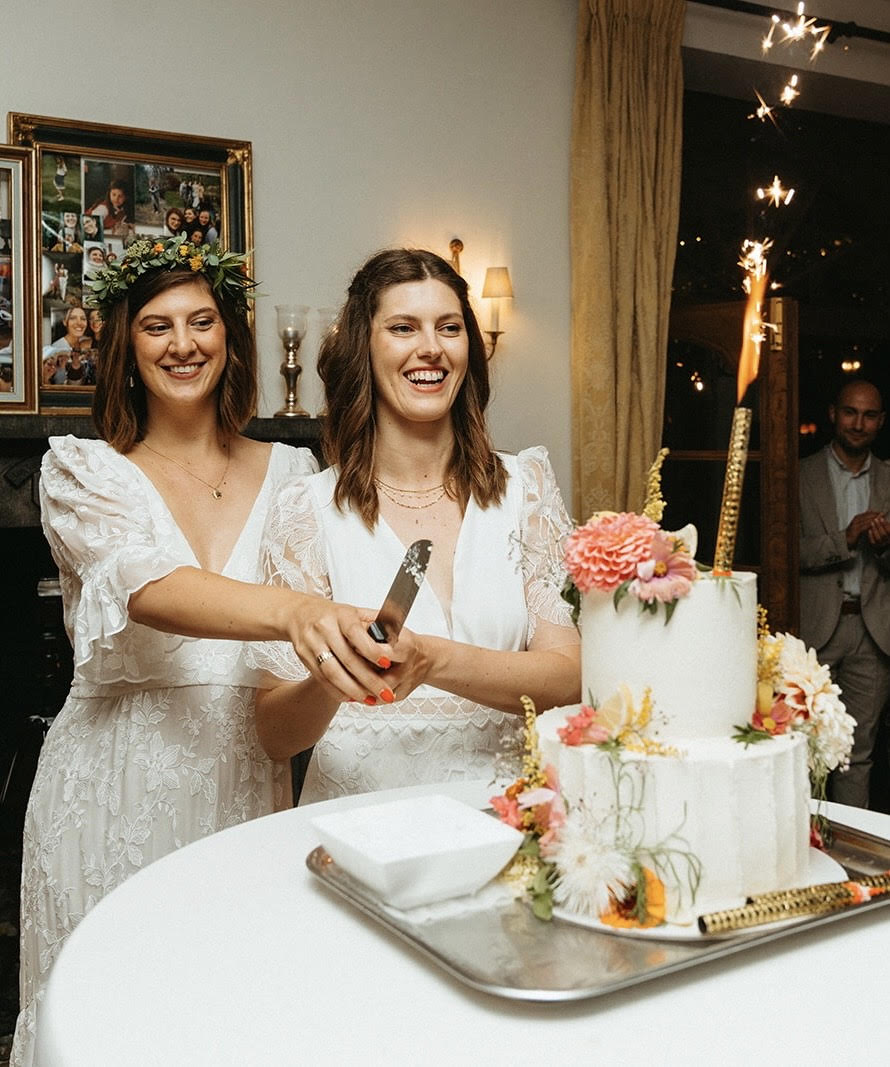 Two women wearing wedding dresses cut their wedding cake together